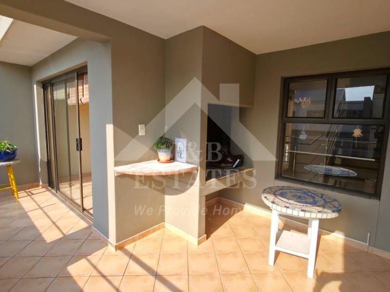Covered patio area featuring a built-in braai, tiled flooring, and sliding door access to the interior living space.