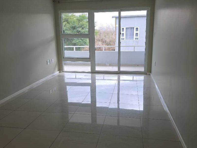 A bright, empty living room featuring polished tiled flooring, recessed lighting, and a large sliding glass door leading to a balcony.