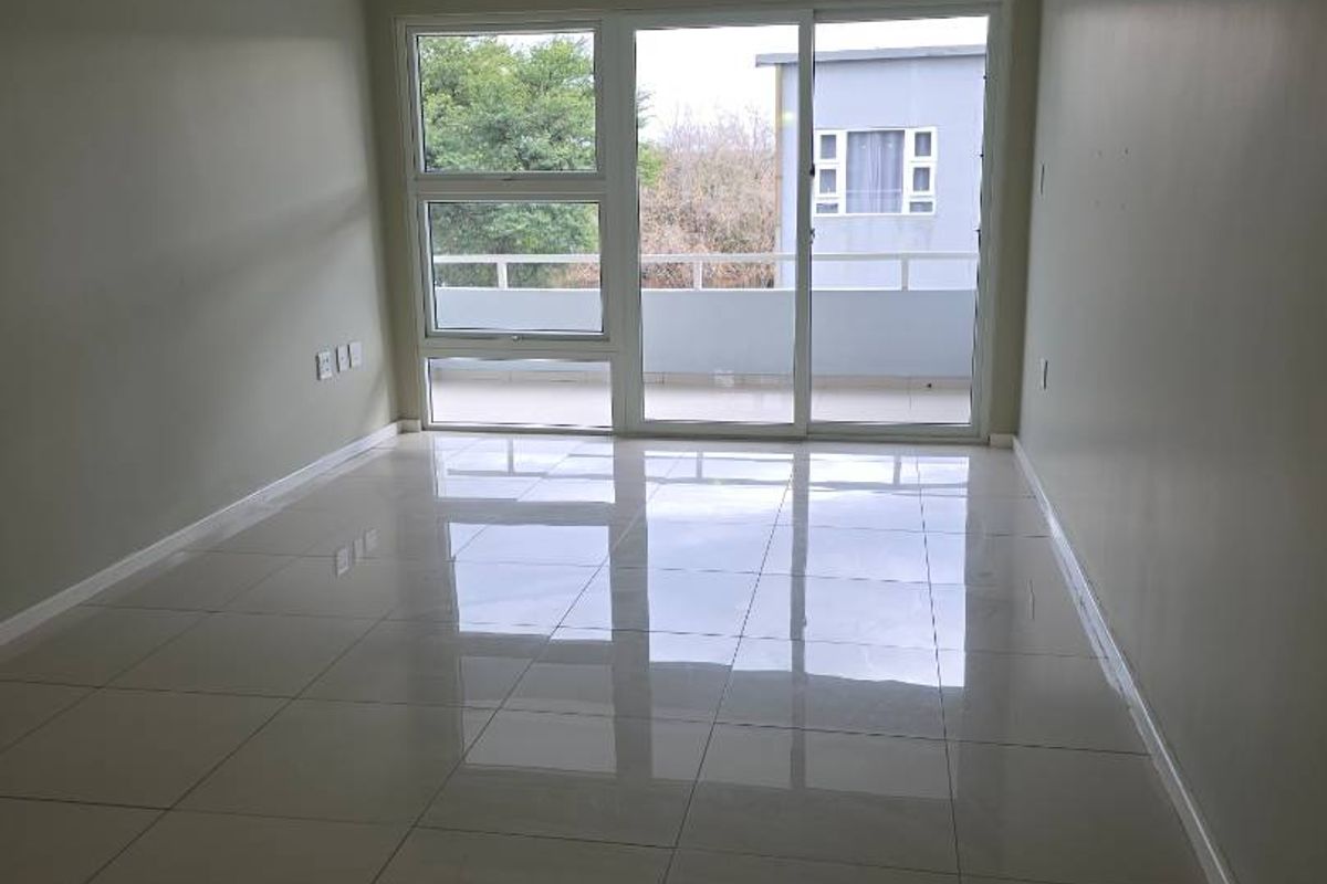 A bright, empty living room featuring polished tiled flooring, recessed lighting, and a large sliding glass door leading to a balcony.