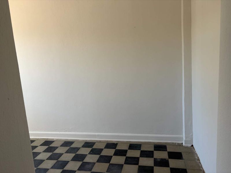 An empty room featuring classic black and white checkerboard tile flooring and plain white walls, offering a blank canvas for renovation.
