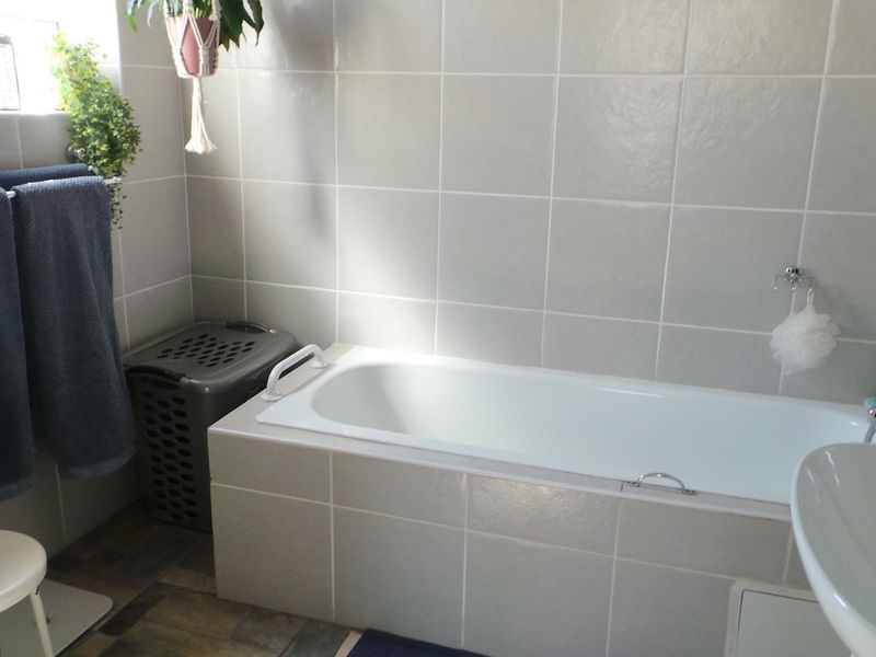 A functional bathroom featuring a built-in bathtub with wall-mounted shower mixer, pedestal basin, and neutral wall tiling.