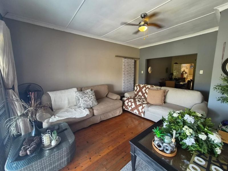 A living room featuring original hardwood flooring, a ceiling fan, and coved ceilings, with an open transition to the adjacent dining area.