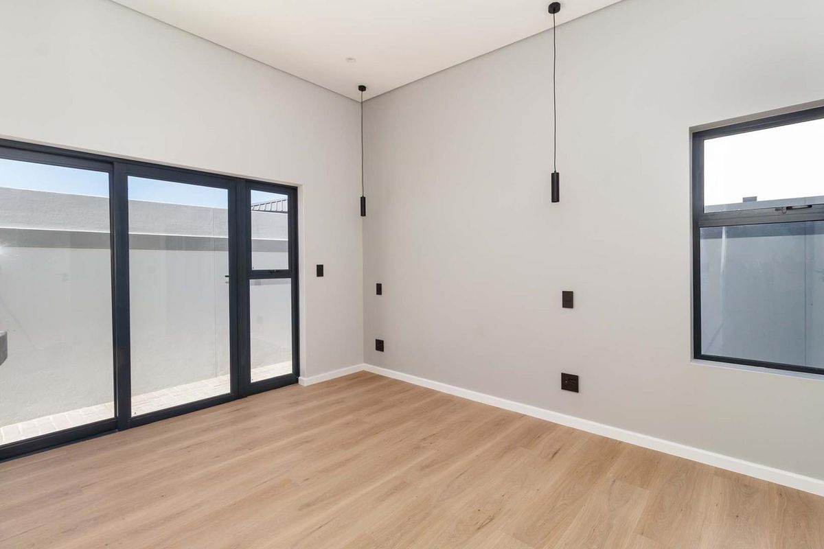 A bright, modern, and empty bedroom featuring light wood-look laminate flooring, sleek black aluminium window and door frames, and contemporary pendant lighting.