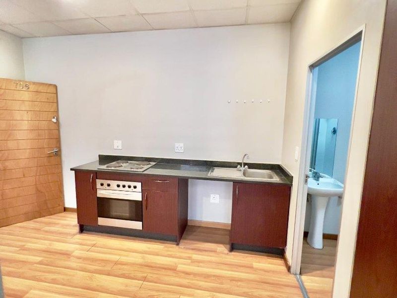 Compact kitchenette featuring built-in oven, hob, and sink, with adjacent bathroom access. The space is vacant and ready for renovation.