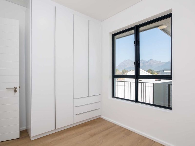 A bright, modern bedroom featuring built-in cupboards, light laminate flooring, and a large window with mountain views.
