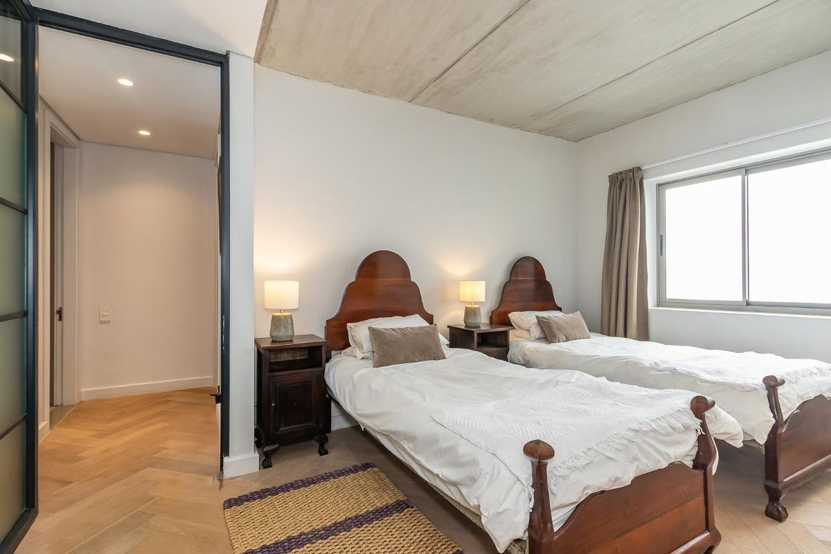 A well-maintained bedroom featuring exposed concrete ceilings, herringbone timber flooring, and a large window providing natural light.