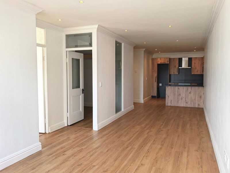 Spacious open-plan living area featuring modern laminate flooring, recessed lighting, and a contemporary kitchen with wood-finish cabinetry and integrated appliances.