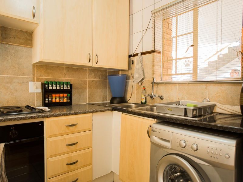 Compact kitchen featuring light wood cabinetry, granite-look laminate countertops, tiled backsplash, and integrated oven and hob with space for a washing machine.