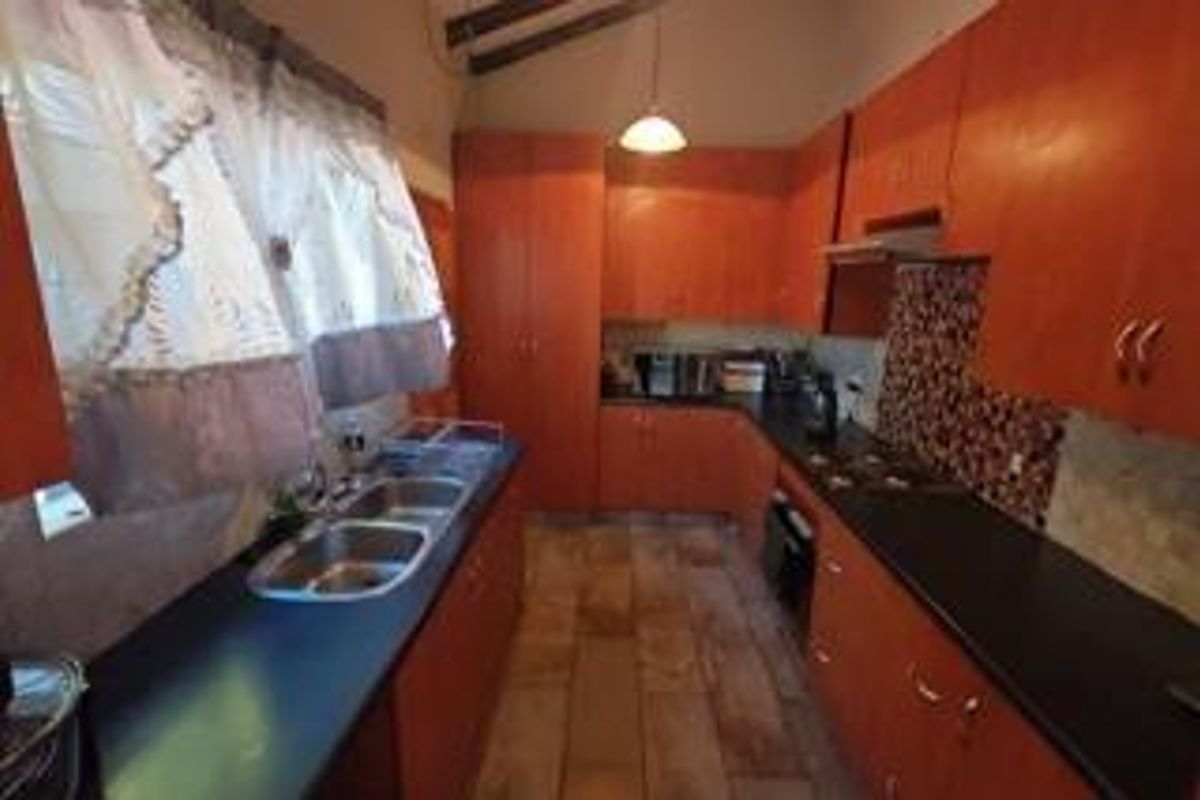 A functional kitchen featuring wooden cabinetry, dark countertops, a double sink, and a tiled backsplash with a built-in oven and hob.