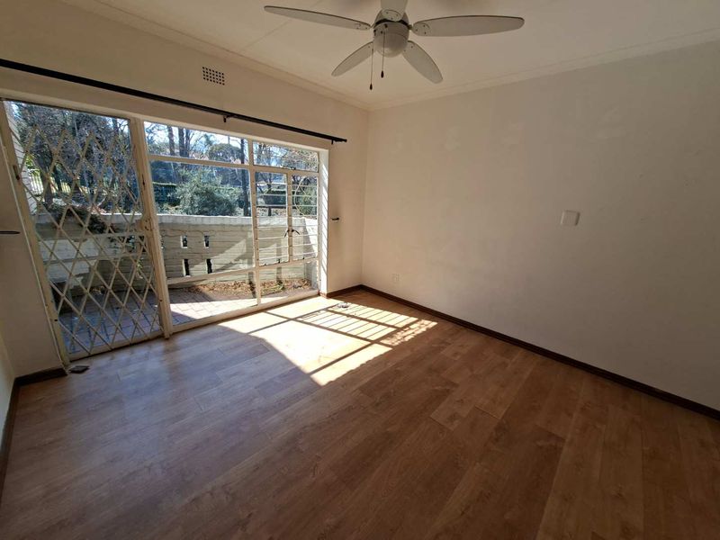 An empty living room featuring laminate flooring, a ceiling fan, and a large sliding glass door providing access to an outdoor patio area.