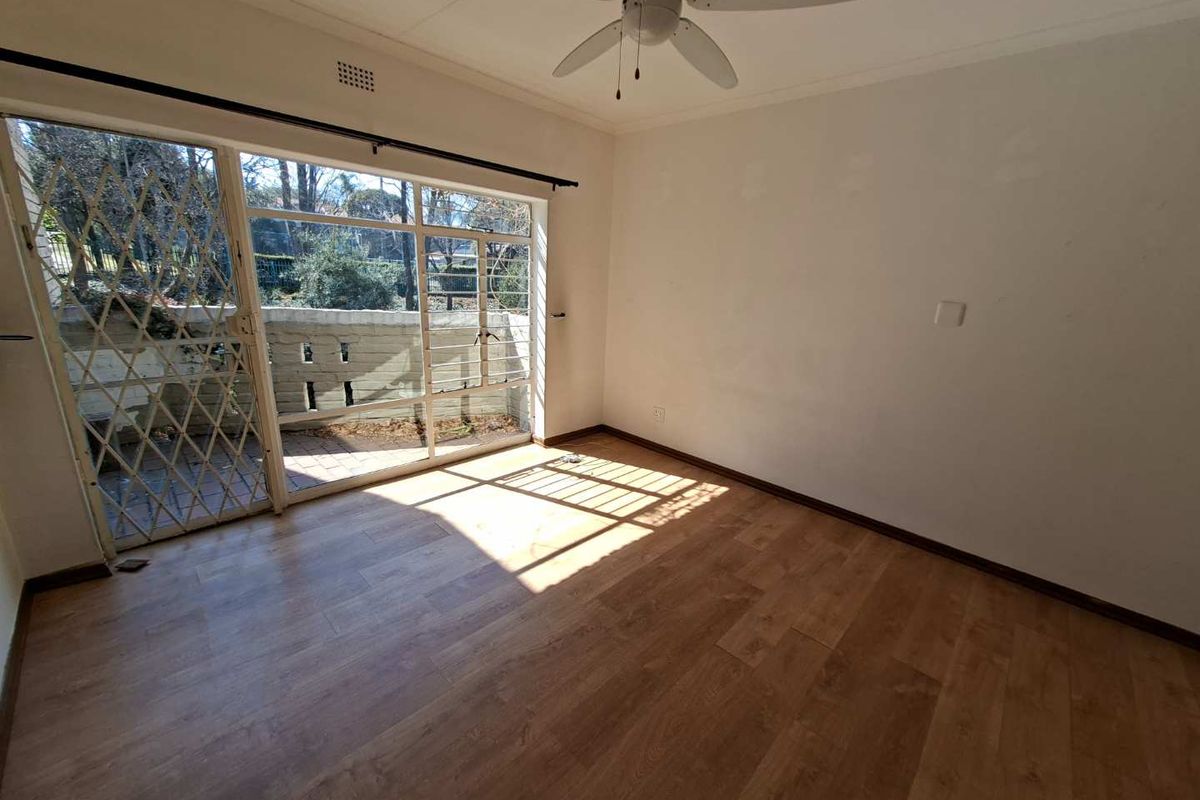 An empty living room featuring laminate flooring, a ceiling fan, and a large sliding glass door providing access to an outdoor patio area.