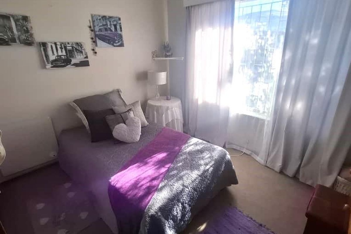 A standard bedroom featuring neutral wall finishes, carpeted flooring, and a large window with curtain treatments.