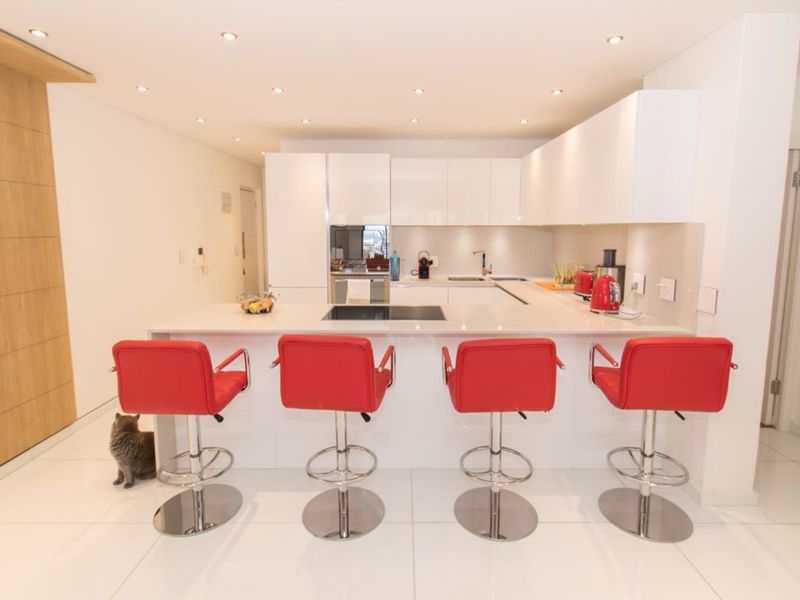 Modern kitchen featuring sleek white cabinetry, stone countertops, integrated hob, and recessed lighting, creating a clean and functional culinary space.