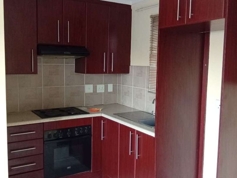 A functional kitchen featuring dark wood-finish cabinetry, built-in oven and hob, tiled backsplash, and neutral floor tiles.