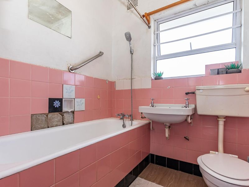 A dated bathroom featuring pink wall tiles, a standard bathtub, wall-mounted basin, and toilet, requiring renovation to update the finishes and fixtures.
