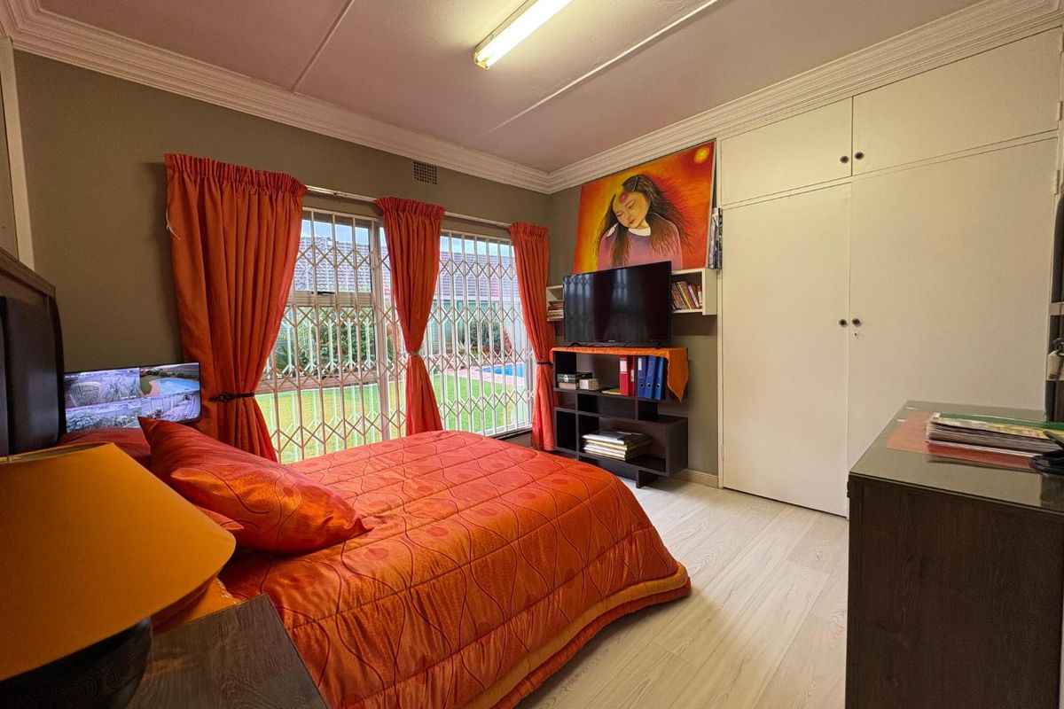 A bedroom featuring built-in cupboards, laminate flooring, and security bars on the windows, providing a functional space with neutral wall tones.