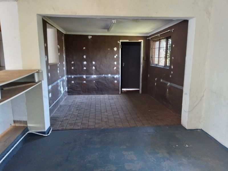 An empty utility space featuring tiled flooring, security bars on the window, and unfinished wall surfaces, offering a blank canvas for renovation.