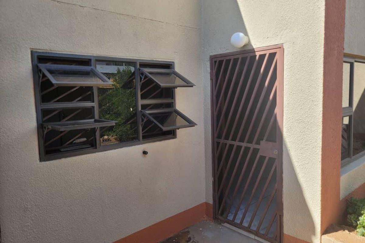 Rear exterior view showing a security gate, top-hung windows, and plastered wall finish with visible signs of wear on the base.