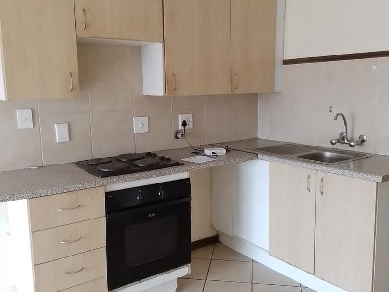 A functional kitchen featuring light wood-tone cabinetry, laminate countertops, a built-in oven with electric hob, and tiled flooring throughout.
