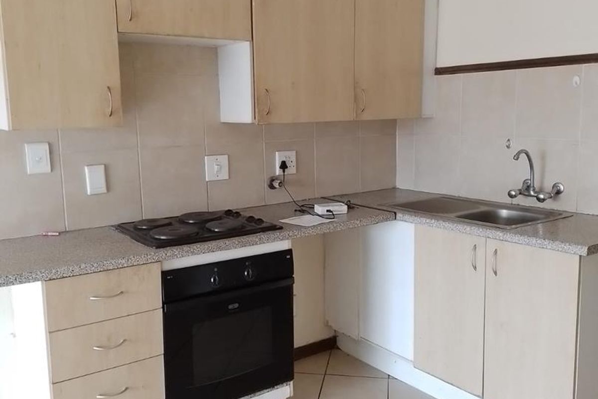 A functional kitchen featuring light wood-tone cabinetry, laminate countertops, a built-in oven with electric hob, and tiled flooring throughout.