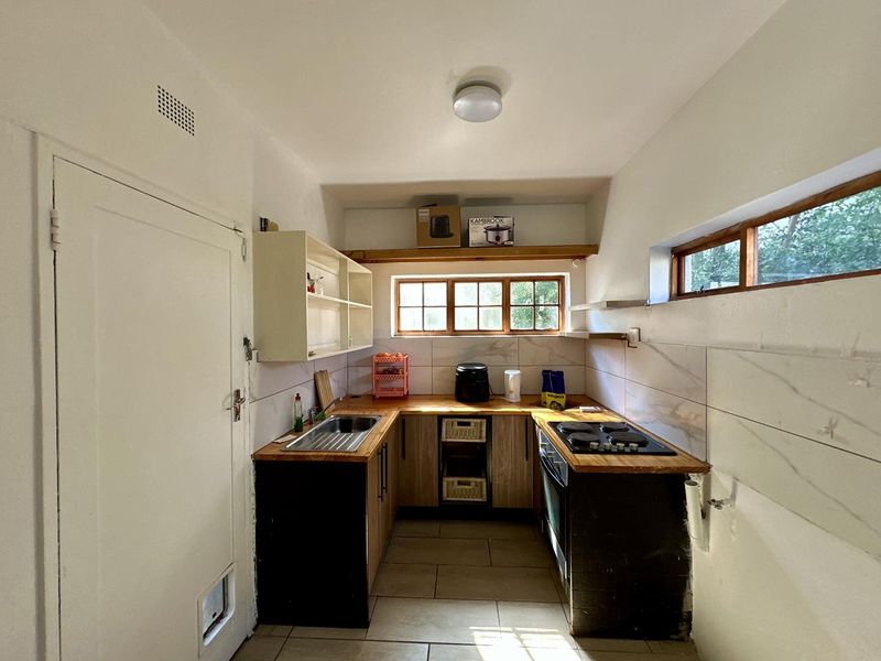 Compact kitchen featuring wooden countertops, built-in oven, electric hob, stainless steel sink, and tiled backsplash with ample storage shelving.