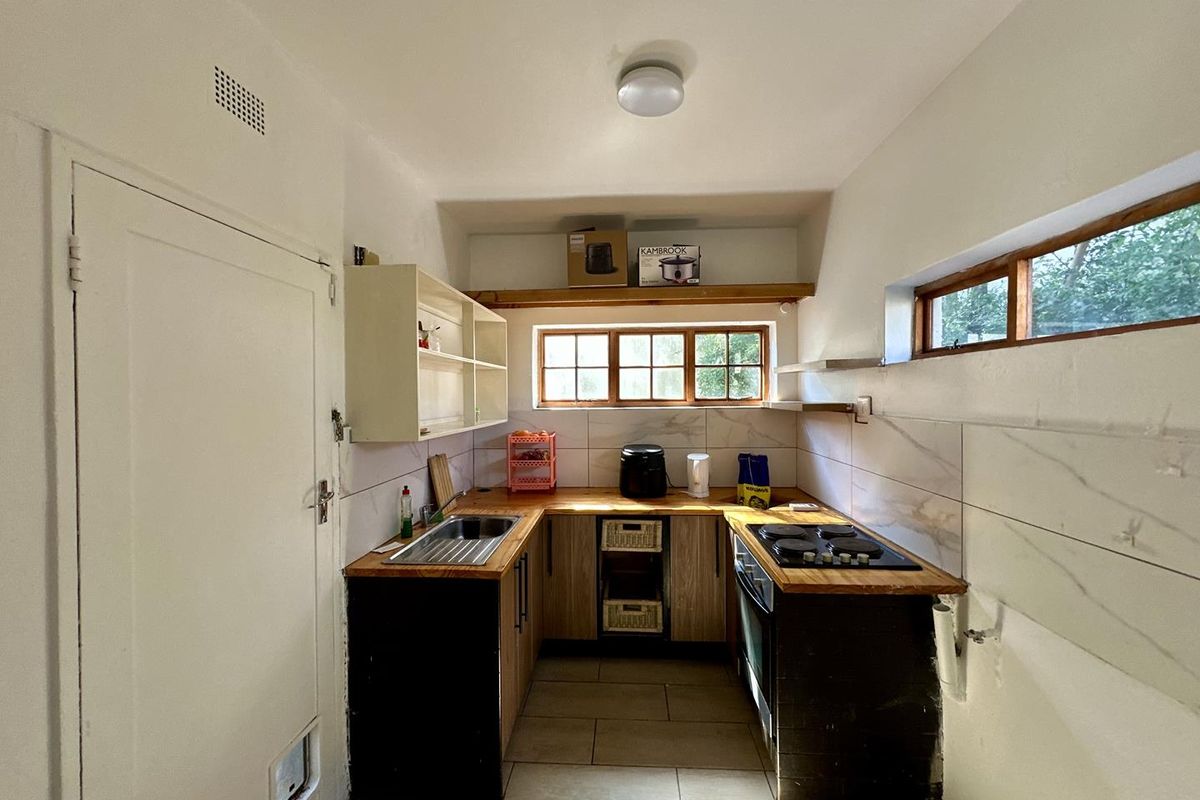 Compact kitchen featuring wooden countertops, built-in oven, electric hob, stainless steel sink, and tiled backsplash with ample storage shelving.
