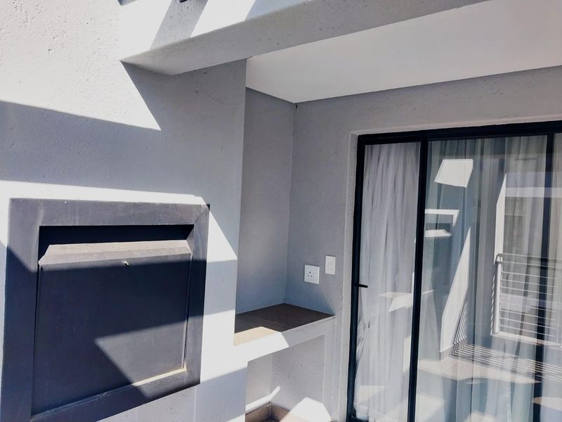 A modern balcony featuring a built-in braai, concrete prep counter, and sliding glass door access to the interior living space.