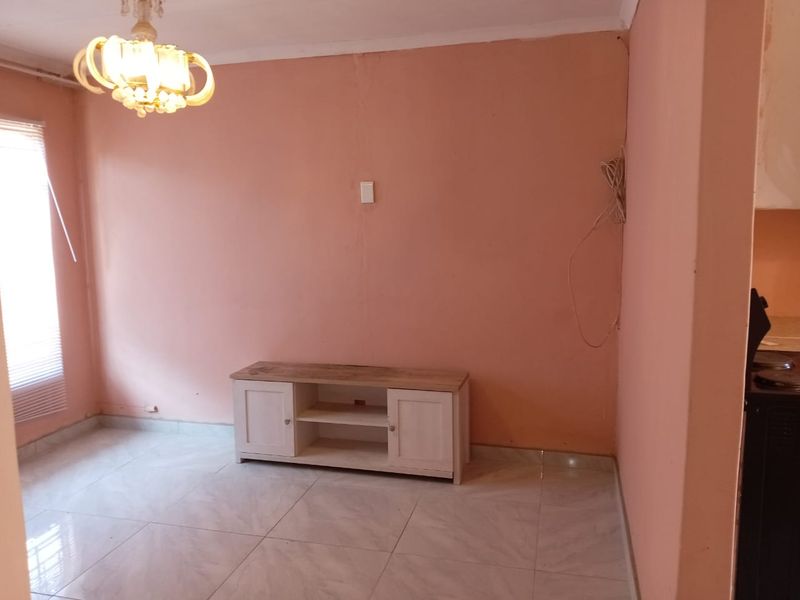 A living room area featuring tiled flooring and a ceiling light fixture, currently requiring cosmetic updates to the wall finishes and electrical tidying.
