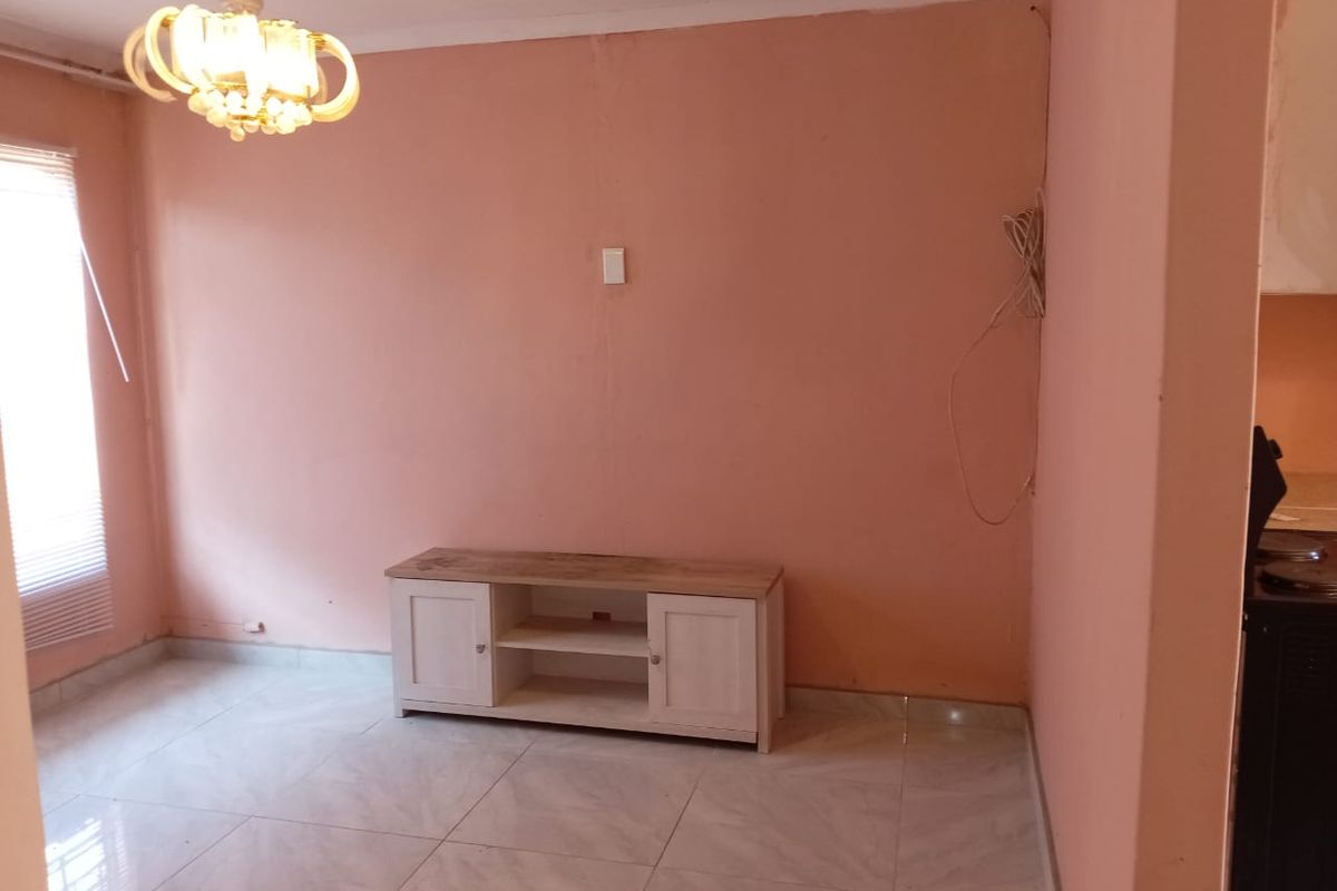 A living room area featuring tiled flooring and a ceiling light fixture, currently requiring cosmetic updates to the wall finishes and electrical tidying.