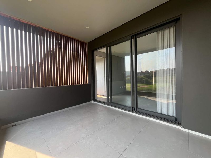 A modern, covered balcony featuring large sliding glass doors, sleek tiled flooring, and a decorative timber slat privacy screen.
