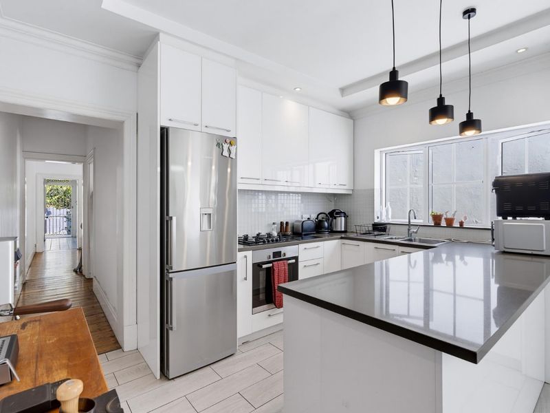 Modern kitchen featuring white cabinetry, stone countertops, integrated gas cooktop, built-in oven, and stylish pendant lighting, offering a clean and functional workspace.