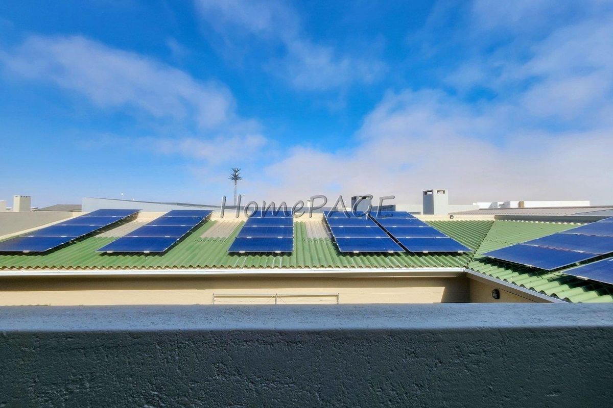 View of a residential roof featuring installed solar panels on a green corrugated metal surface.