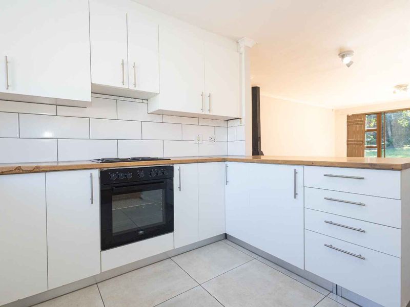 A clean, modern kitchen featuring white cabinetry, wooden countertops, a built-in oven, and a subway tile backsplash, opening into an adjacent living area.