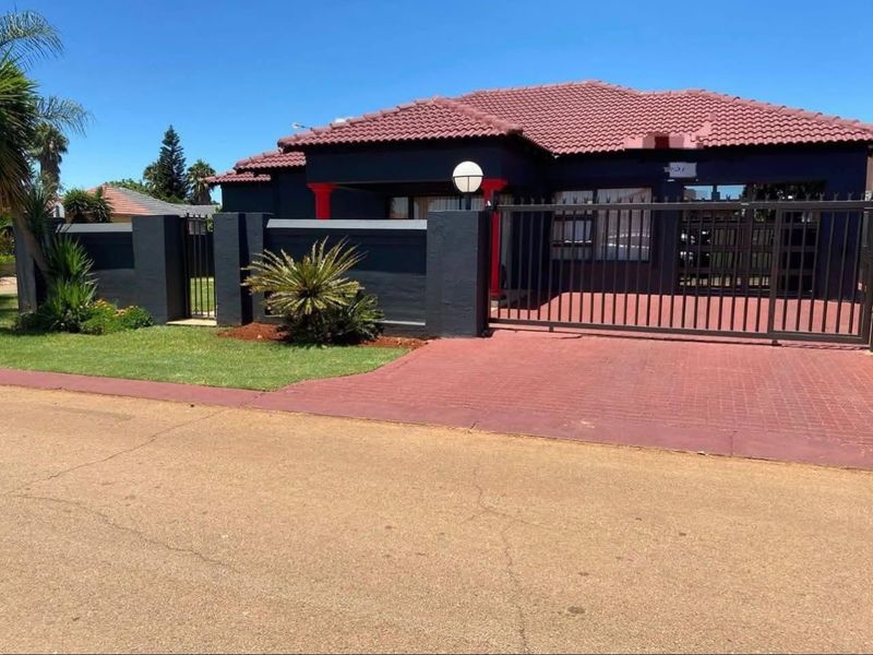 Front elevation of a well-maintained house featuring a dark exterior finish, tiled roof, secure perimeter wall, and a paved driveway with a sliding gate.