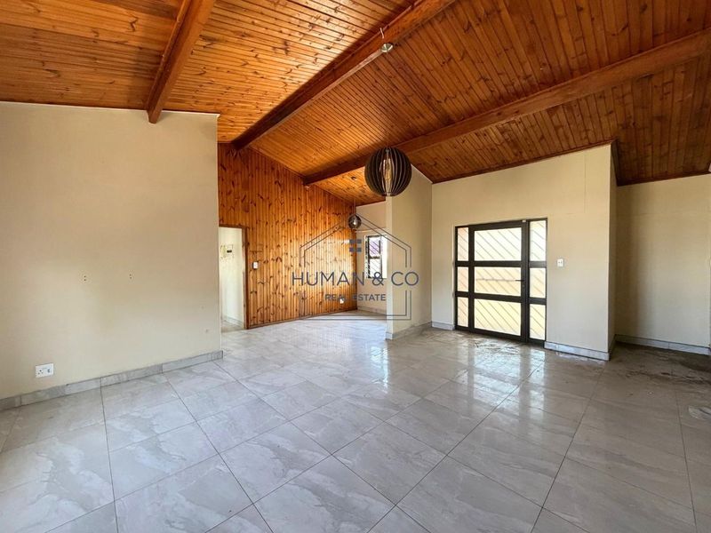 Spacious living area featuring a high vaulted timber ceiling, warm wood wall paneling, and neutral tiled flooring with a glass-paneled entrance door.