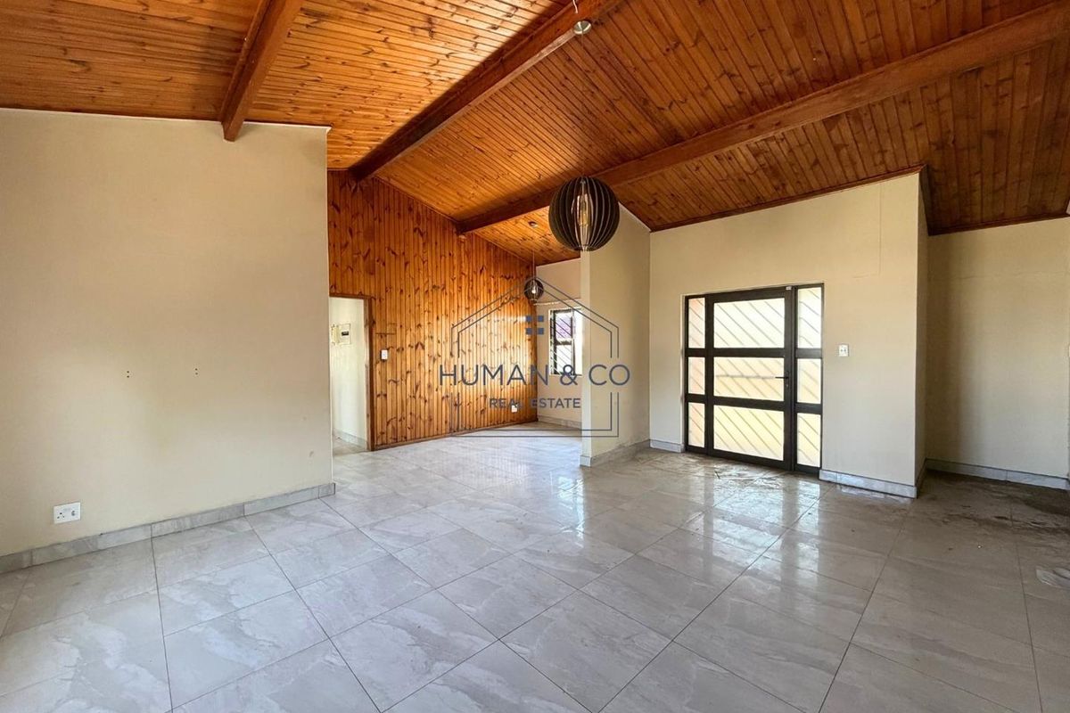 Spacious living area featuring a high vaulted timber ceiling, warm wood wall paneling, and neutral tiled flooring with a glass-paneled entrance door.