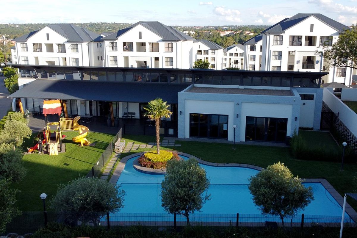 Aerial view of a residential apartment complex featuring a communal swimming pool, landscaped garden, children's play area, and modern building architecture.