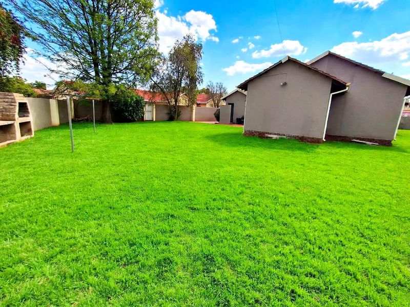 Spacious rear garden featuring a well-maintained lawn, perimeter walling, and a built-in outdoor braai area.