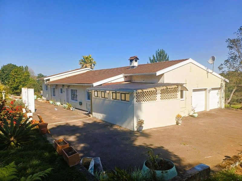 Rear view of a single-story house featuring a tiled roof, chimney, double garage, and a paved driveway with a covered patio area.