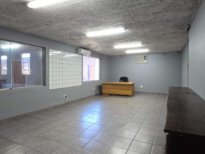 Spacious industrial office area featuring tiled flooring, fluorescent lighting, air conditioning, and a large interior window for natural light.