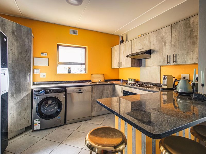 Functional kitchen featuring granite countertops, built-in cabinetry, gas hob, extractor fan, and integrated space for laundry appliances, finished with tiled flooring.
