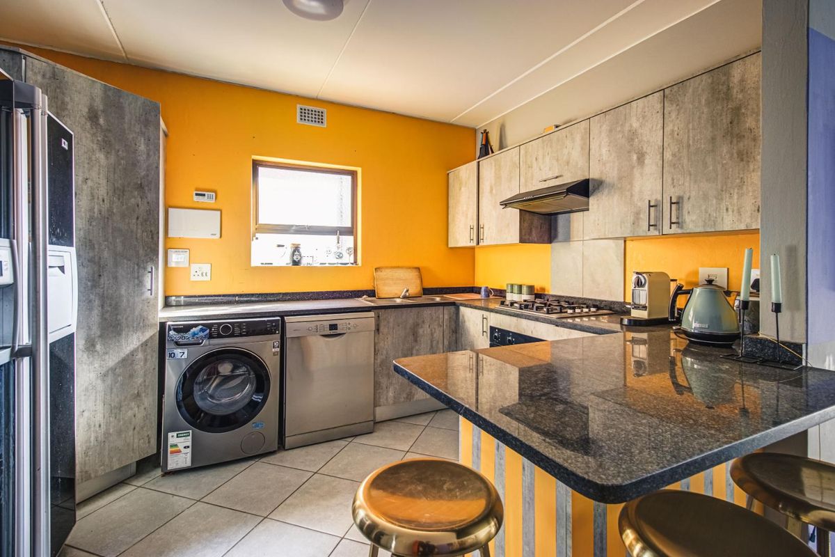 Functional kitchen featuring granite countertops, built-in cabinetry, gas hob, extractor fan, and integrated space for laundry appliances, finished with tiled flooring.