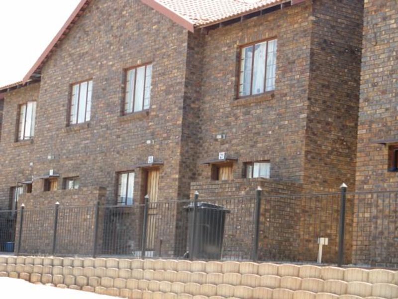 Exterior view of a multi-unit apartment complex featuring face brick construction, tiled roofing, and secure perimeter fencing.