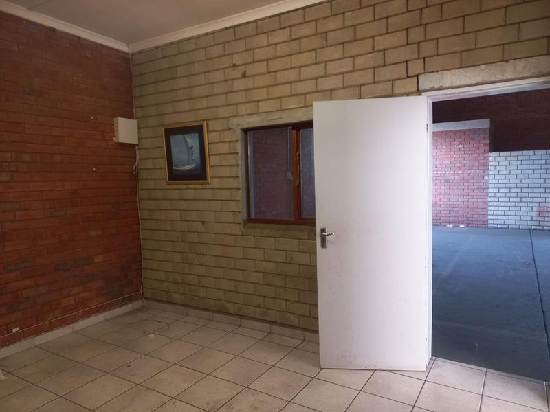An empty utility space featuring exposed brick walls, tiled flooring, and a connecting doorway leading to an adjacent industrial area.
