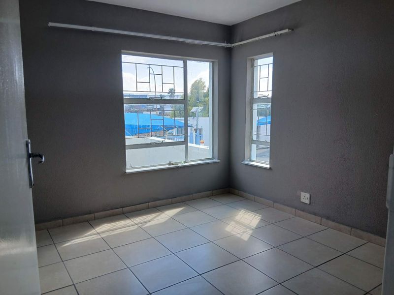 An empty bedroom featuring tiled flooring, grey painted walls, and windows fitted with security bars, offering a blank canvas for personalization.