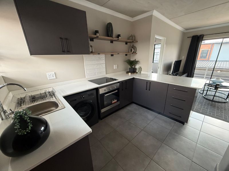 Modern open-plan kitchen featuring dark cabinetry, stone countertops, integrated appliances, and tiled flooring, seamlessly flowing into the adjacent living area.