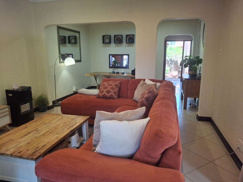 A living room featuring tiled flooring and arched doorways leading to an adjacent dining area and rear access.