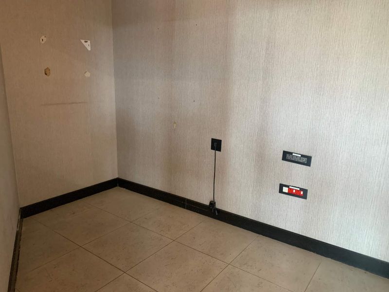 An empty office space featuring tiled flooring, textured wallpaper, and integrated electrical and data connectivity points, showing minor wall surface wear.