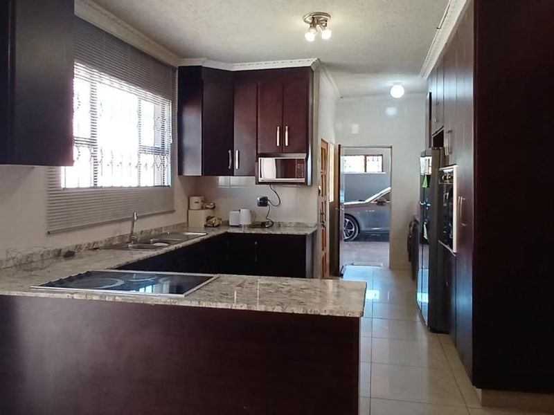 A functional kitchen featuring dark wood cabinetry, granite countertops, built-in appliances, and tiled flooring, offering a clean and practical workspace.