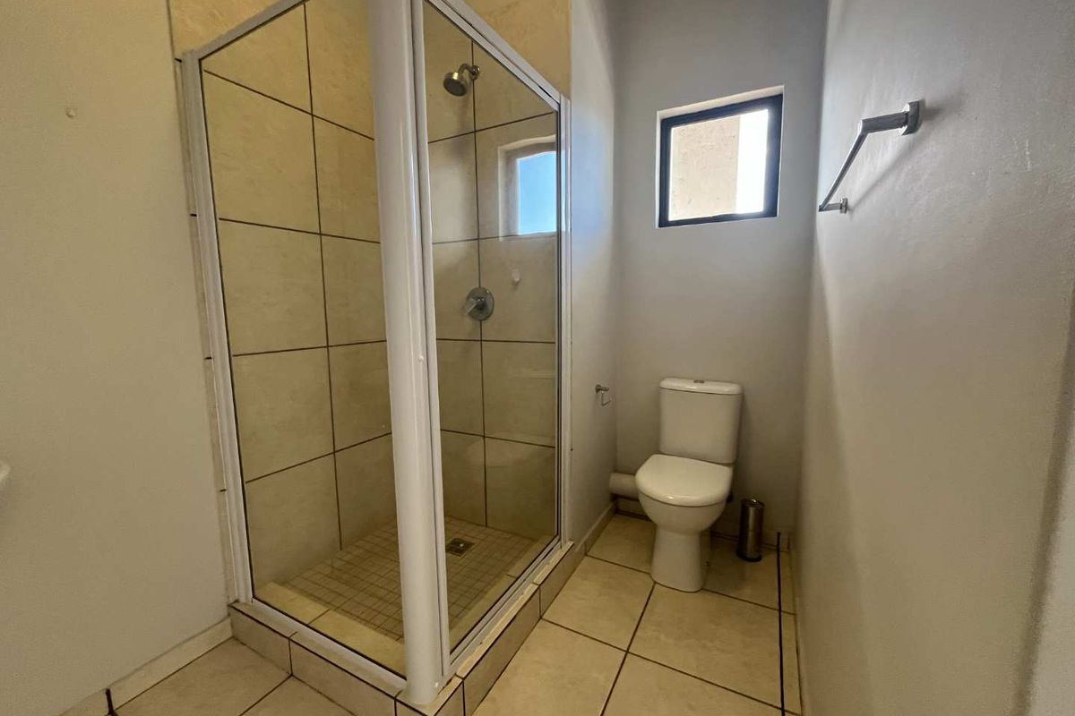 A functional bathroom featuring a glass-enclosed shower with tiled walls and a standard white toilet.